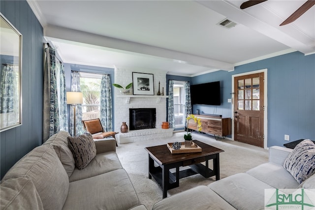 living room featuring beamed ceiling, a fireplace, light carpet, ornamental molding, and ceiling fan