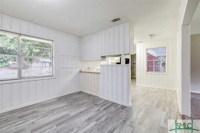 empty room with light wood-style floors, baseboards, visible vents, and wooden walls