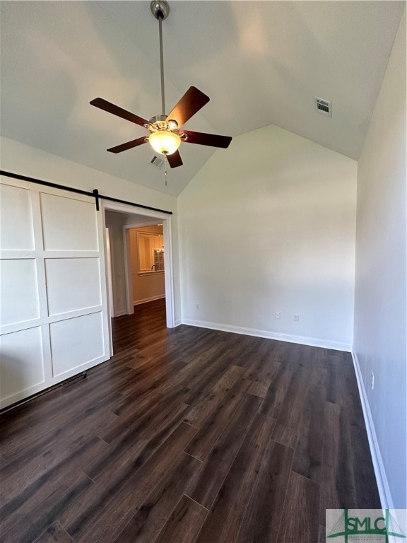 unfurnished bedroom with a barn door, ceiling fan, dark hardwood / wood-style floors, and vaulted ceiling