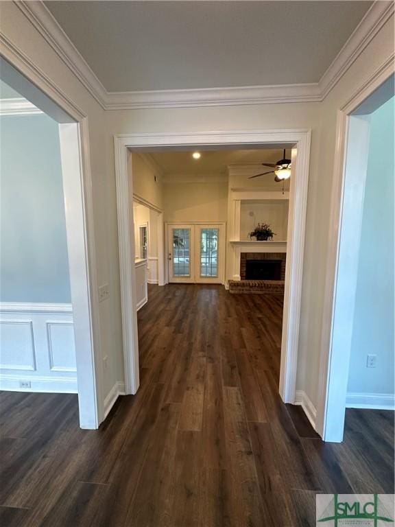 corridor with a wainscoted wall, crown molding, and dark wood-type flooring