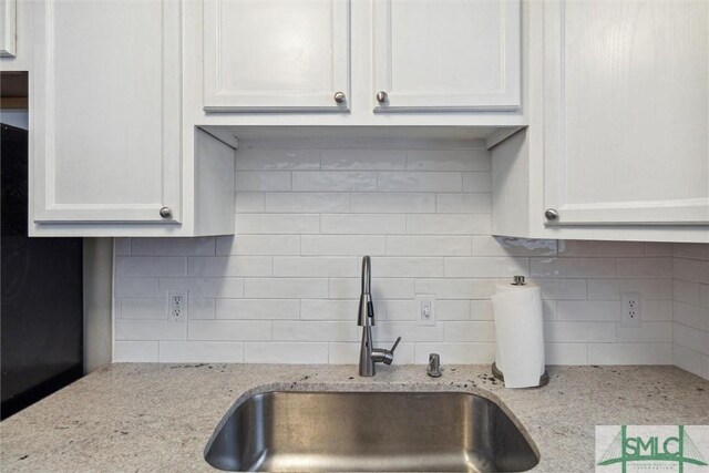 kitchen with white cabinetry, light stone counters, sink, and backsplash