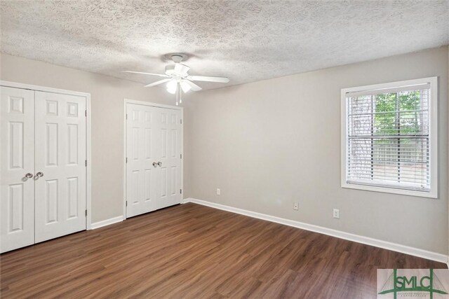 unfurnished bedroom with two closets, ceiling fan, dark hardwood / wood-style floors, and a textured ceiling