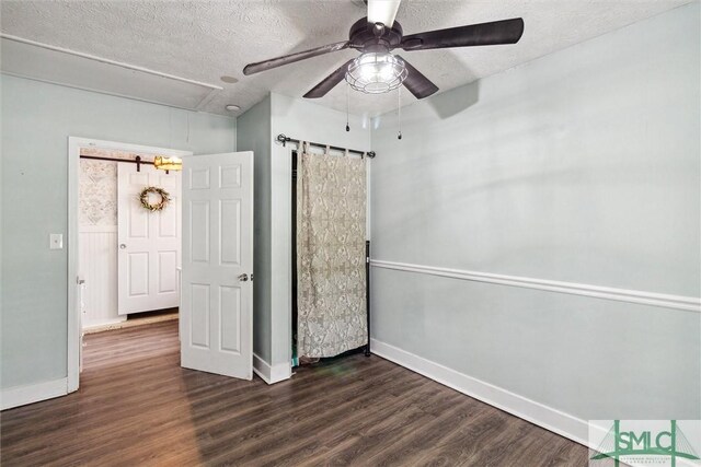 unfurnished bedroom with dark wood-type flooring, ceiling fan, a barn door, and a textured ceiling