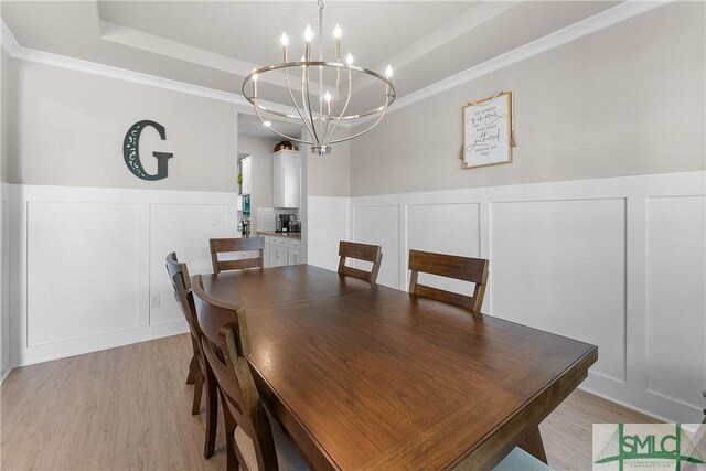 dining area with a raised ceiling, a notable chandelier, and light hardwood / wood-style floors