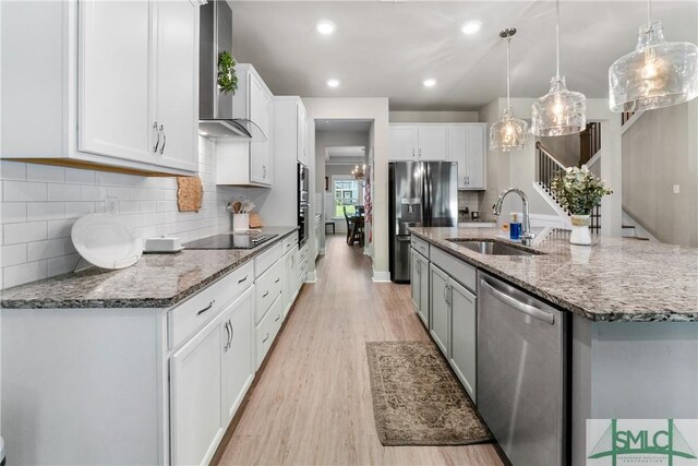 kitchen with wall chimney range hood, appliances with stainless steel finishes, decorative backsplash, and light hardwood / wood-style floors