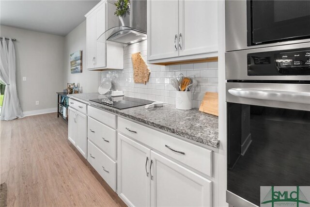 kitchen featuring backsplash, oven, wall chimney range hood, black electric cooktop, and light hardwood / wood-style floors