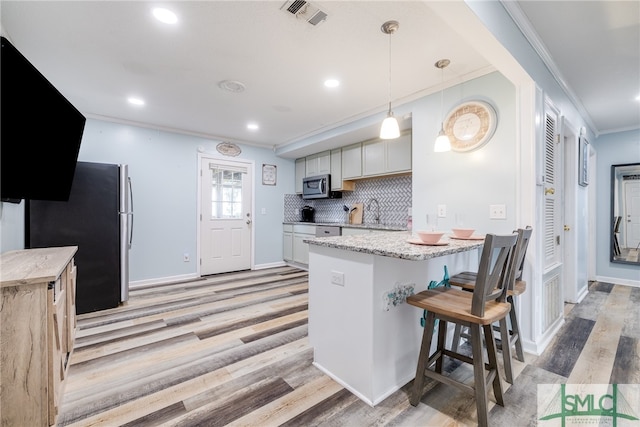 kitchen featuring a kitchen bar, stainless steel appliances, tasteful backsplash, and light hardwood / wood-style flooring