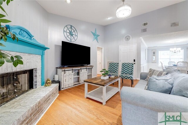 living room with a high ceiling, an inviting chandelier, a fireplace, and light hardwood / wood-style floors