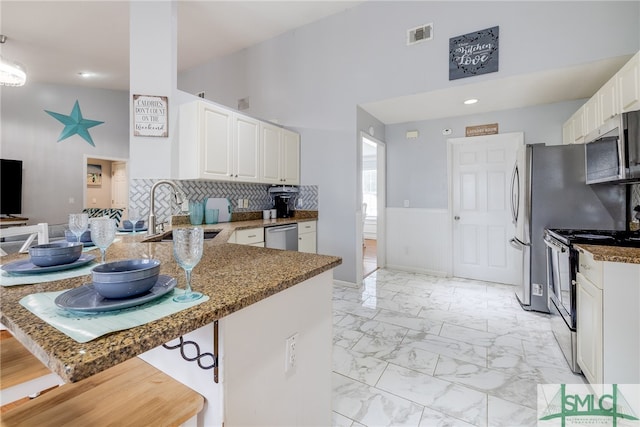 kitchen featuring dark stone countertops, appliances with stainless steel finishes, sink, kitchen peninsula, and tasteful backsplash