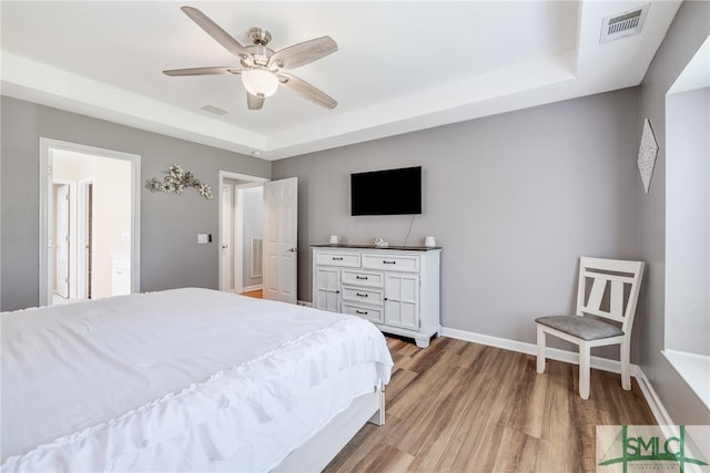 bedroom with ceiling fan, connected bathroom, a tray ceiling, and light hardwood / wood-style floors