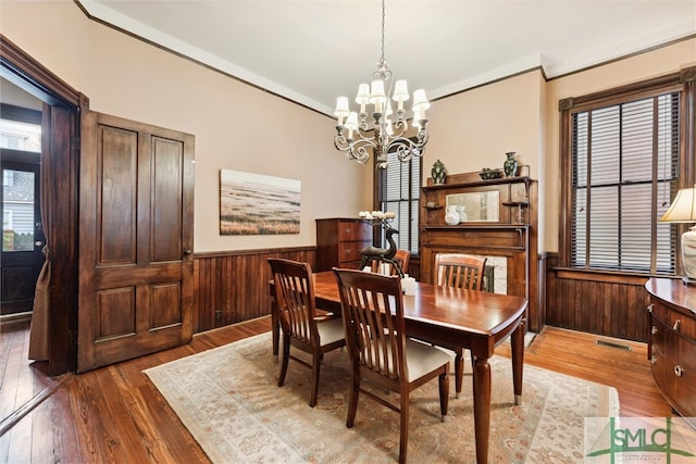 dining room featuring hardwood / wood-style flooring, wooden walls, a notable chandelier, and ornamental molding