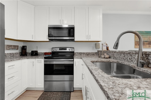 kitchen featuring ornamental molding, white cabinetry, stainless steel appliances, sink, and light hardwood / wood-style floors