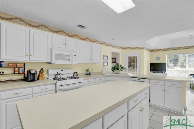 kitchen with a textured ceiling, a kitchen island, white appliances, light tile patterned floors, and white cabinetry