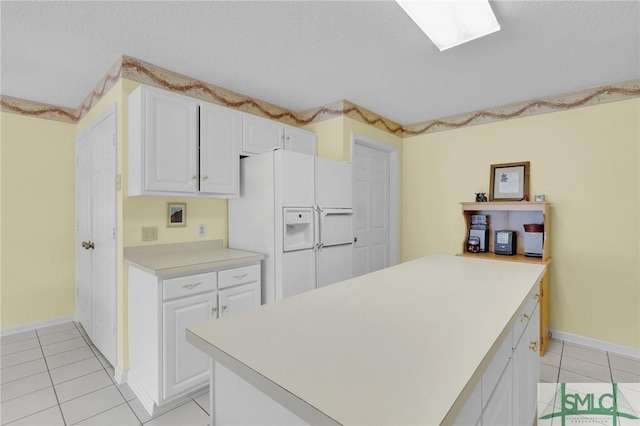 kitchen with light tile patterned floors, white refrigerator with ice dispenser, white cabinets, a peninsula, and light countertops