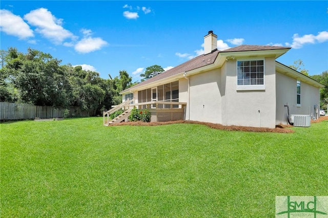 back of property with central AC unit, fence, a sunroom, a lawn, and a chimney