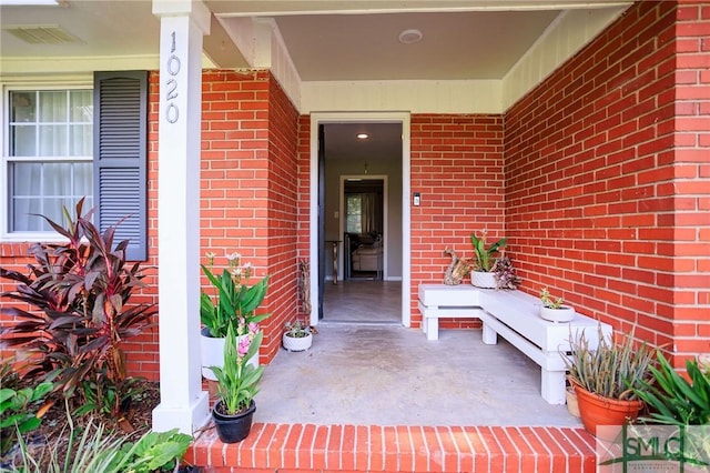 doorway to property with covered porch and brick siding