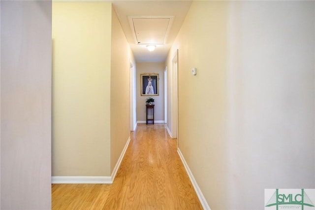 hall with light wood finished floors, attic access, and baseboards