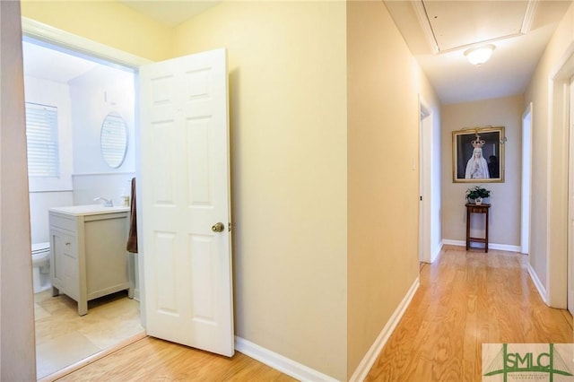 hall featuring attic access, light wood-style floors, baseboards, and a sink