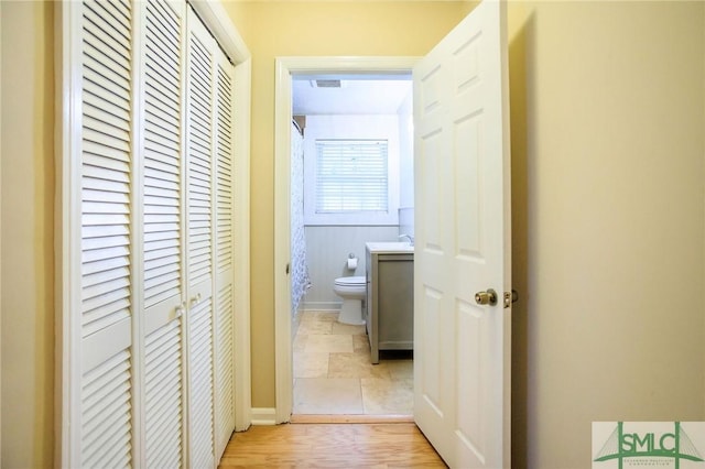 hall featuring visible vents, stone finish floor, baseboards, and a sink