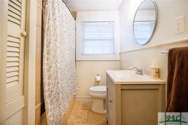 full bath featuring a shower with shower curtain, a wainscoted wall, toilet, and vanity