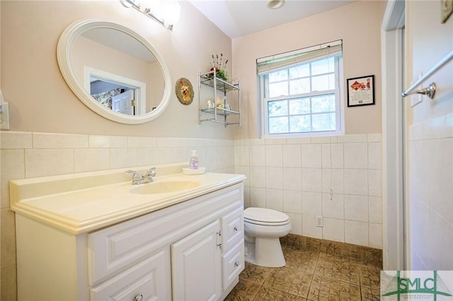 bathroom featuring vanity, tile walls, toilet, and wainscoting