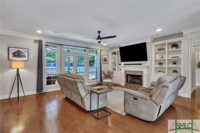 living room featuring a fireplace, hardwood / wood-style floors, built in features, ornamental molding, and ceiling fan