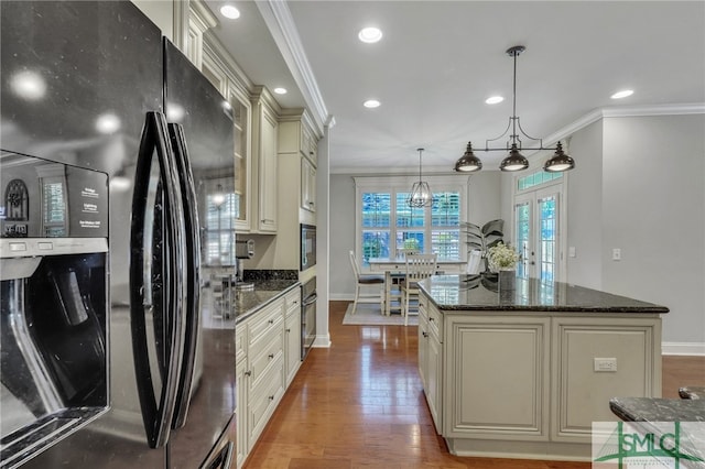 kitchen with wood-type flooring, black refrigerator, cream cabinetry, pendant lighting, and a kitchen island