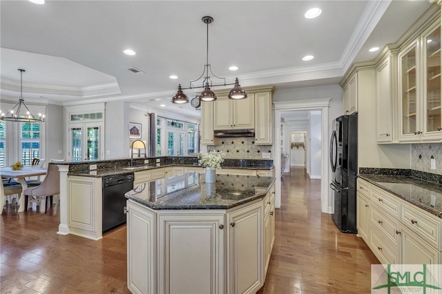 kitchen with black appliances, wood-type flooring, decorative light fixtures, and cream cabinetry