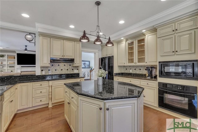 kitchen featuring light wood finished floors, glass insert cabinets, cream cabinets, under cabinet range hood, and black appliances