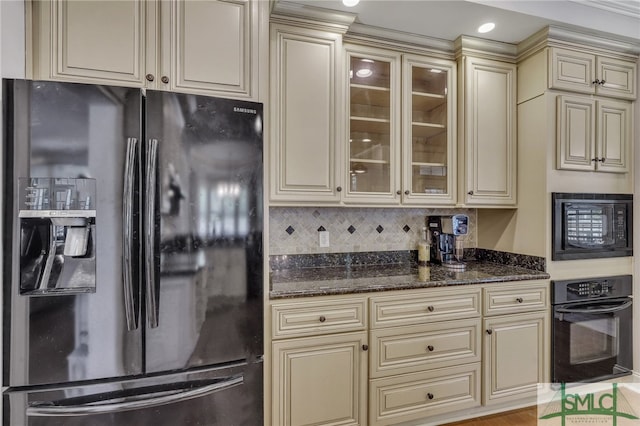 kitchen with backsplash, dark stone countertops, light wood-type flooring, black appliances, and cream cabinetry