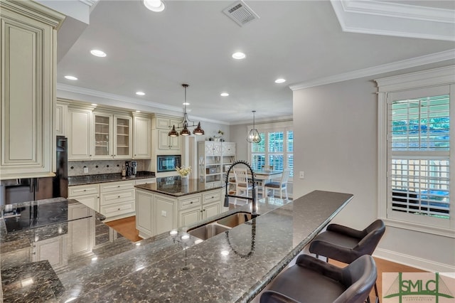 kitchen featuring cream cabinets, a center island, sink, dark stone counters, and pendant lighting