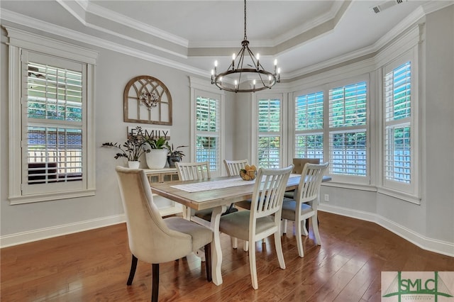 dining area with a tray ceiling, dark wood-type flooring, ornamental molding, and an inviting chandelier