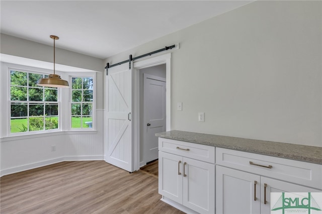 kitchen featuring a barn door, decorative light fixtures, white cabinets, and light hardwood / wood-style floors