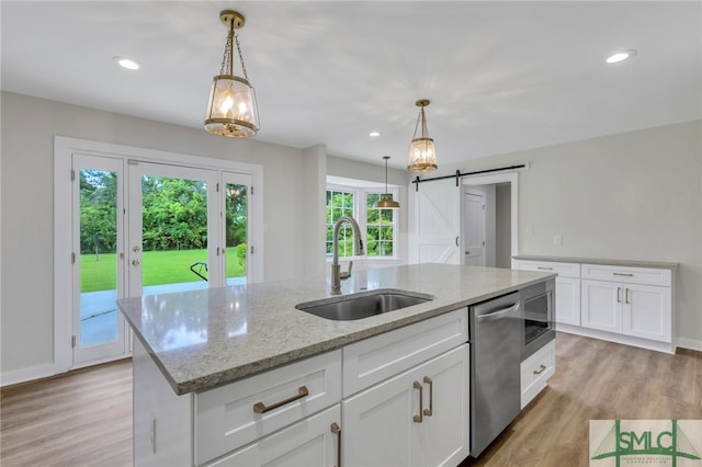 kitchen with a barn door, sink, light wood-type flooring, and a kitchen island with sink