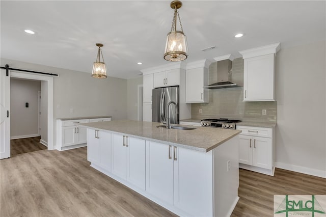 kitchen with wall chimney exhaust hood, a center island with sink, sink, a barn door, and white cabinets