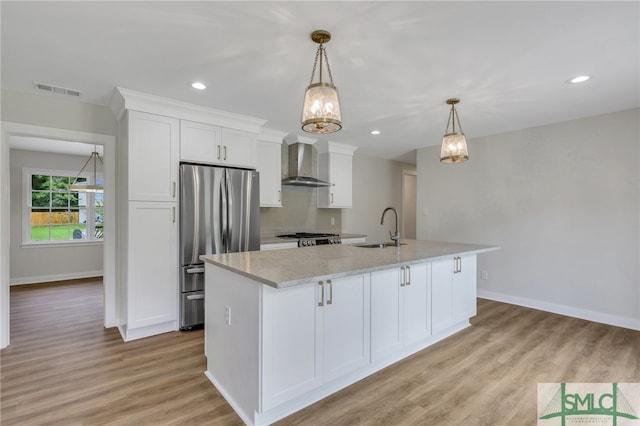 kitchen with appliances with stainless steel finishes, a kitchen island with sink, sink, white cabinetry, and wall chimney range hood