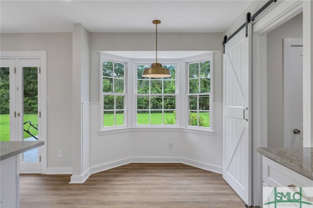 unfurnished dining area featuring plenty of natural light, a barn door, and light hardwood / wood-style floors