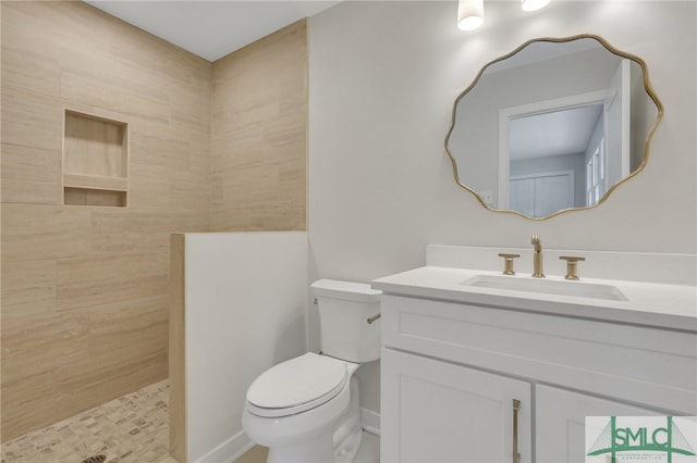 bathroom featuring toilet, a tile shower, and vanity