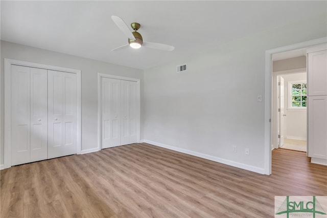 unfurnished bedroom with hardwood / wood-style floors, two closets, and ceiling fan