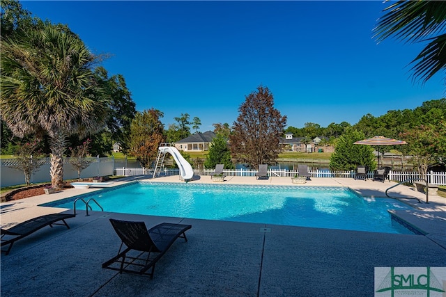 view of pool featuring a water view, a water slide, a diving board, and a patio