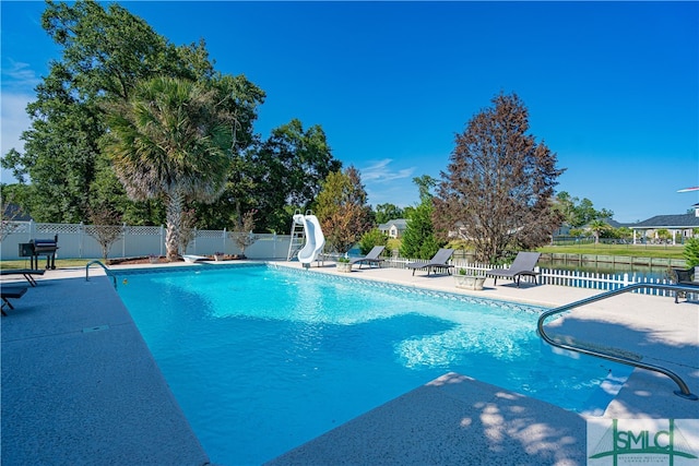 view of swimming pool with a water slide, a diving board, and a patio