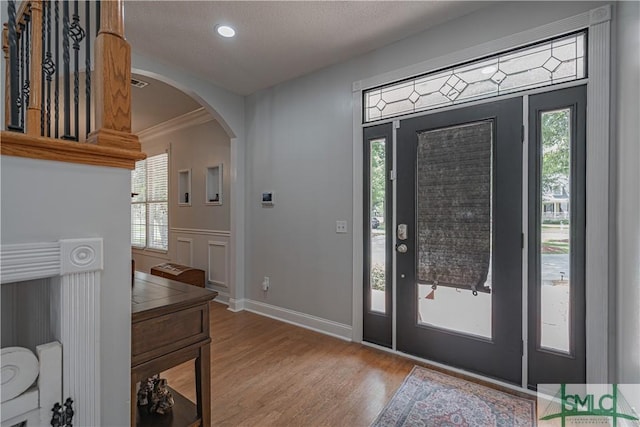 foyer entrance with arched walkways, plenty of natural light, wood finished floors, and crown molding