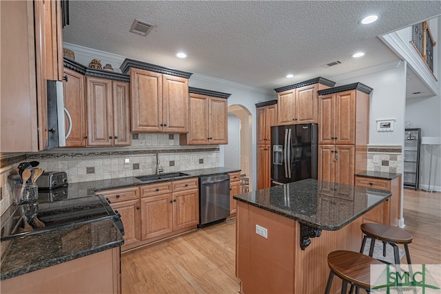 kitchen with light wood-type flooring, appliances with stainless steel finishes, a center island, and dark stone counters