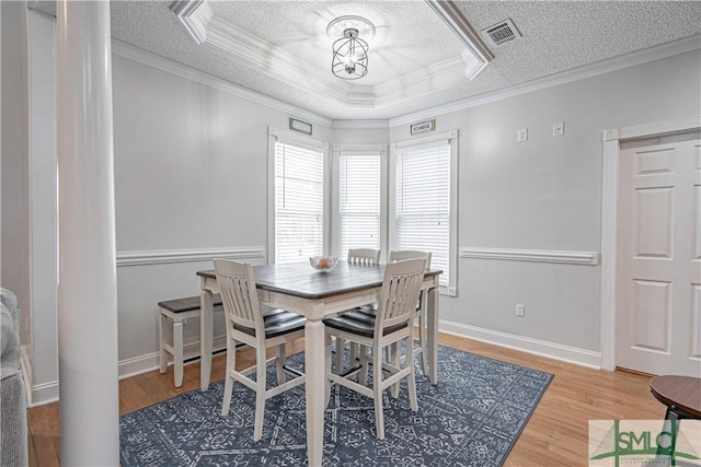 dining space with light wood-type flooring, visible vents, a raised ceiling, and a textured ceiling