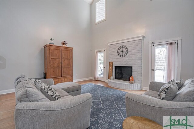 living room featuring a fireplace, light wood-type flooring, a healthy amount of sunlight, and a high ceiling