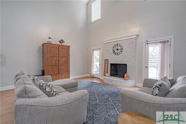 living area featuring a brick fireplace, wood finished floors, a towering ceiling, and baseboards