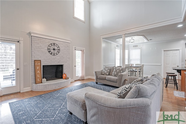 living room featuring a fireplace, crown molding, light wood-type flooring, ceiling fan, and a textured ceiling