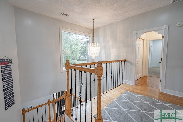 hallway featuring a textured ceiling, a chandelier, wood finished floors, visible vents, and an upstairs landing