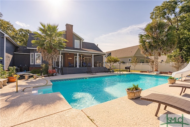 view of swimming pool with a water slide, a diving board, and a patio