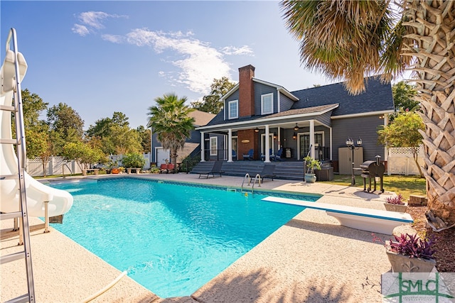 view of swimming pool with a water slide, a patio area, and a diving board